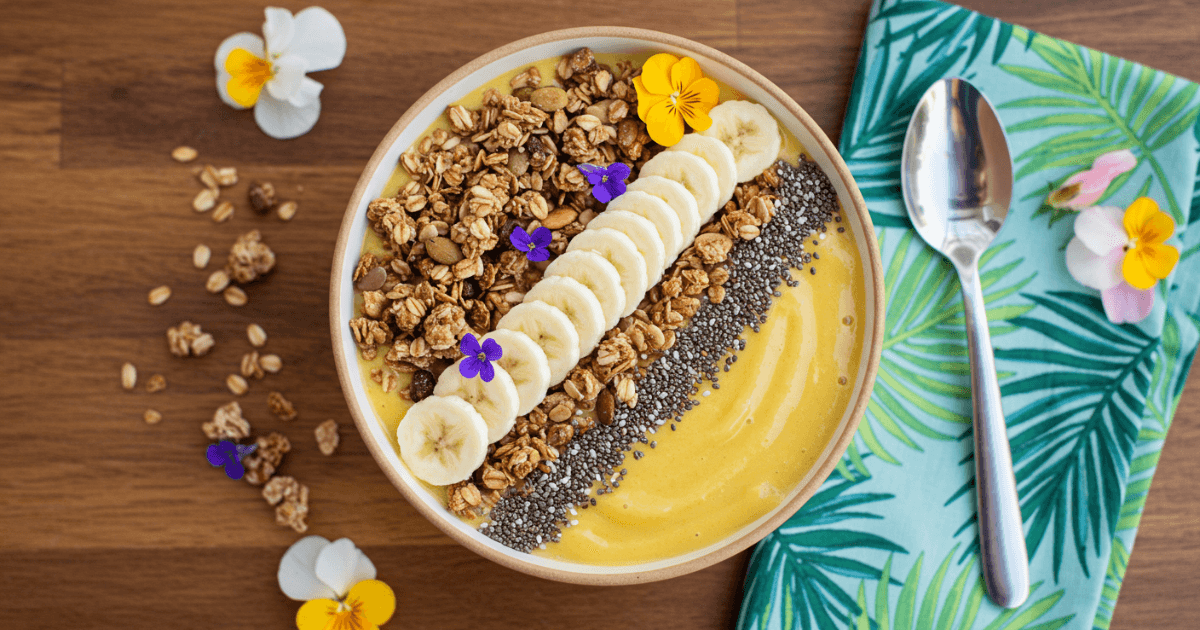 A mango smoothie bowl topped with granola, banana slices, and coconut flakes, styled for a fresh and nutritious look.