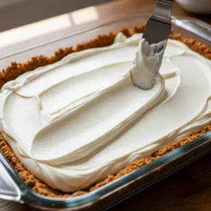 Cream cheese mixture spread over a pretzel crust to form the creamy middle layer of strawberry pretzel dessert.