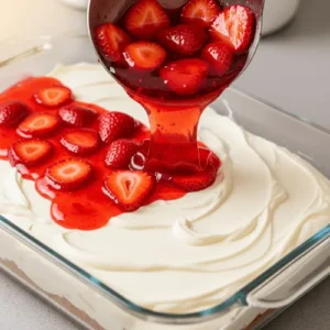 Strawberry Jell-O mixture with sliced strawberries being poured over the creamy layer of strawberry pretzel dessert.