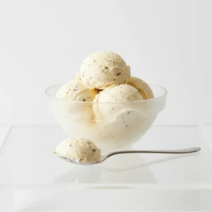A scoop of creamy vanilla ice cream with visible vanilla bean specks in a bowl on a white table.