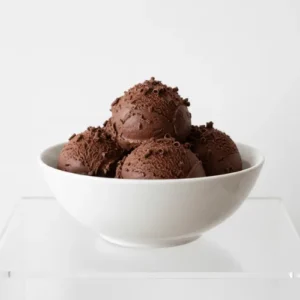Scoops of dark chocolate ice cream topped with chocolate shavings in a bowl on a white table.