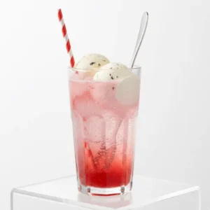A tall glass of strawberry ice cream soda with vanilla ice cream, pink syrup, and fizzy bubbles on a white table.