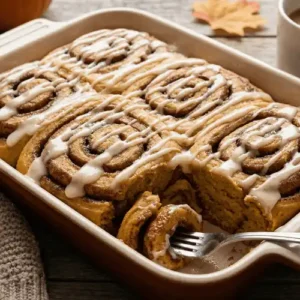 A soft pumpkin cinnamon roll cake swirled with cinnamon sugar and topped with a glossy icing drizzle. Perfect for showcasing rich fall flavors in dessert posts.