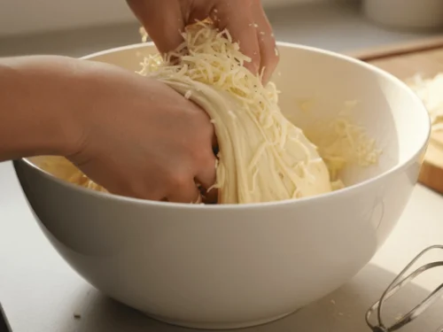 Grated cheese being mixed into elastic Brazilian cheese bread dough by hand.