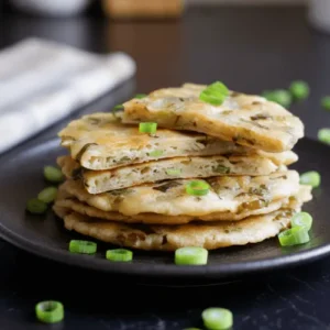 Crispy Chinese scallion pancakes stacked on a plate, showing flaky layers and a golden crust. Perfect example of homemade pan-fried scallion pancakes.