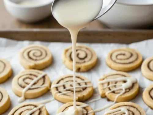 Vanilla glaze being drizzled over freshly baked cinnamon roll cookies for a sweet finishing touch.