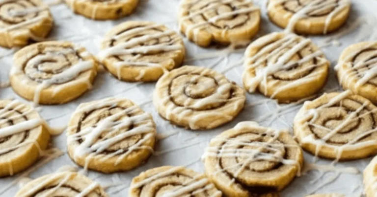 Cinnamon roll cookies with visible cinnamon swirls and vanilla glaze cooling on a baking sheet. These cookies resemble classic cinnamon rolls in cookie form.