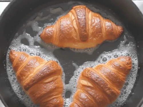 Croissant French toast cooking in a skillet with butter until golden brown. A crucial step for achieving crisp edges.