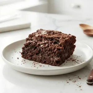 A fudgy cottage cheese brownie square served on a dessert plate with a fork, showing its rich chocolate texture.