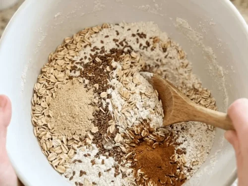A large mixing bowl filled with oats, flour, flaxseed, and brewer’s yeast being whisked together. These ingredients form the base of lactation cookies.